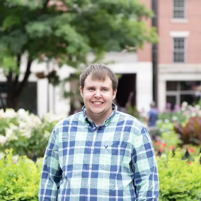 Young man standing outdoors and smiling at camera in plaid shirt