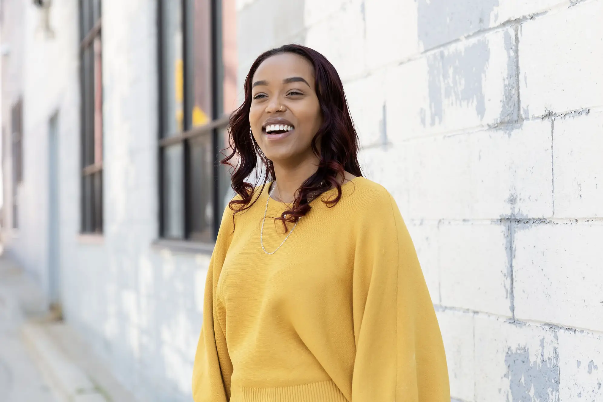 Woman in yellow sweater laughing in front of painted brick wall