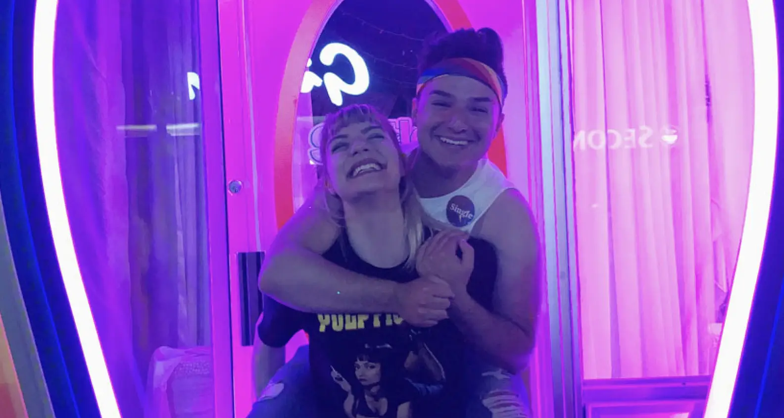 Two people smiling and hugging with a pink and purple background