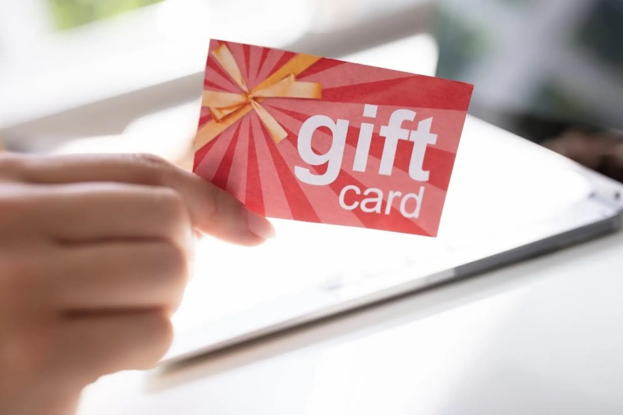 A hand holding up a red piece of paper that says "gift" card" in large type