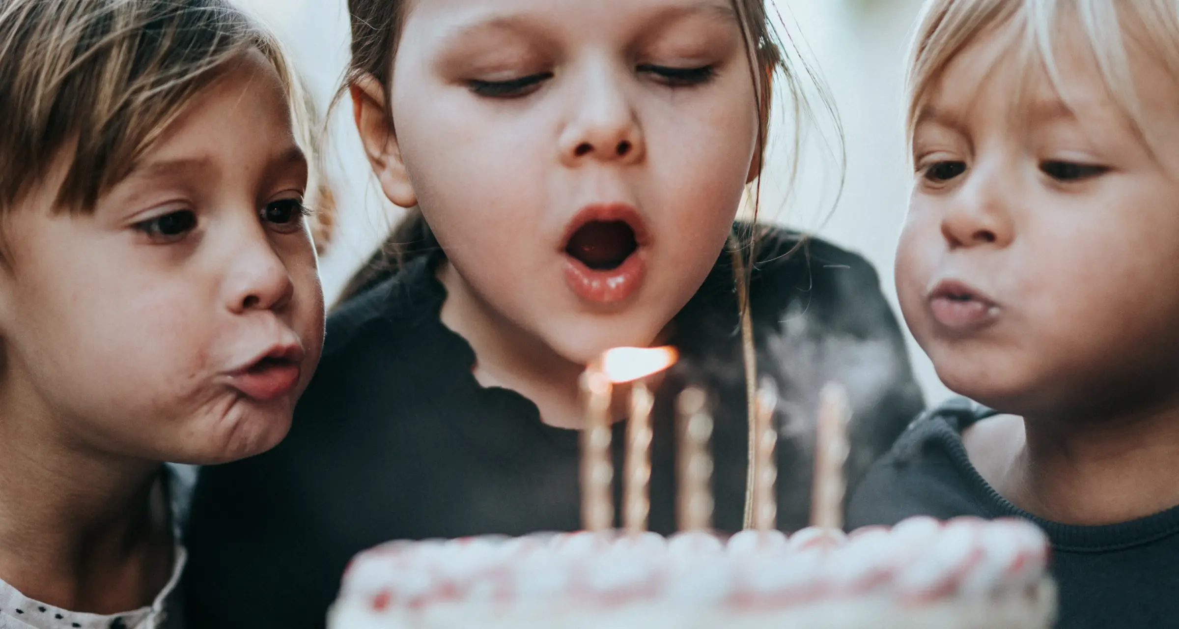 Three children blowing the candles out on a birthday cake
