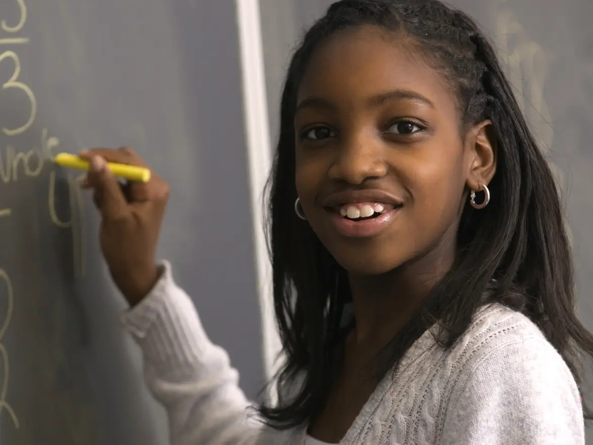 Girl smiling at camera while writing in yellow chalk on a chalkboard