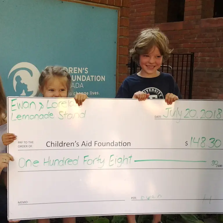 Two smiling children holding an oversized check