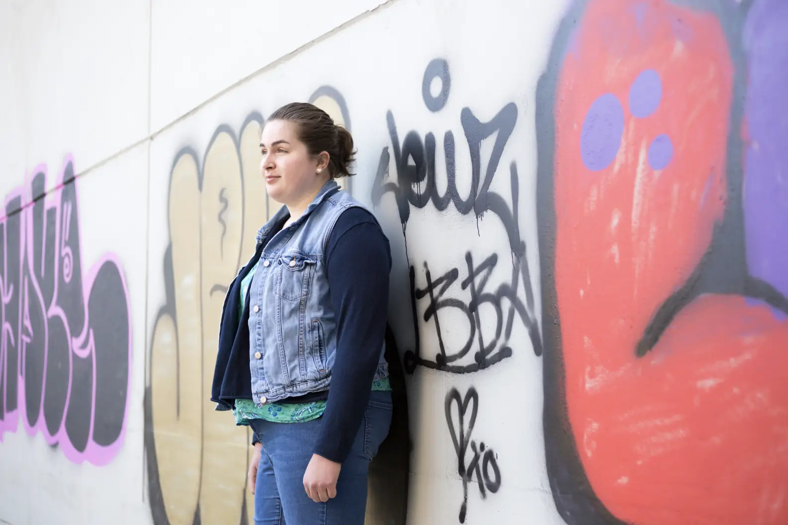 Young woman leaning against a wall that has graffiti on it