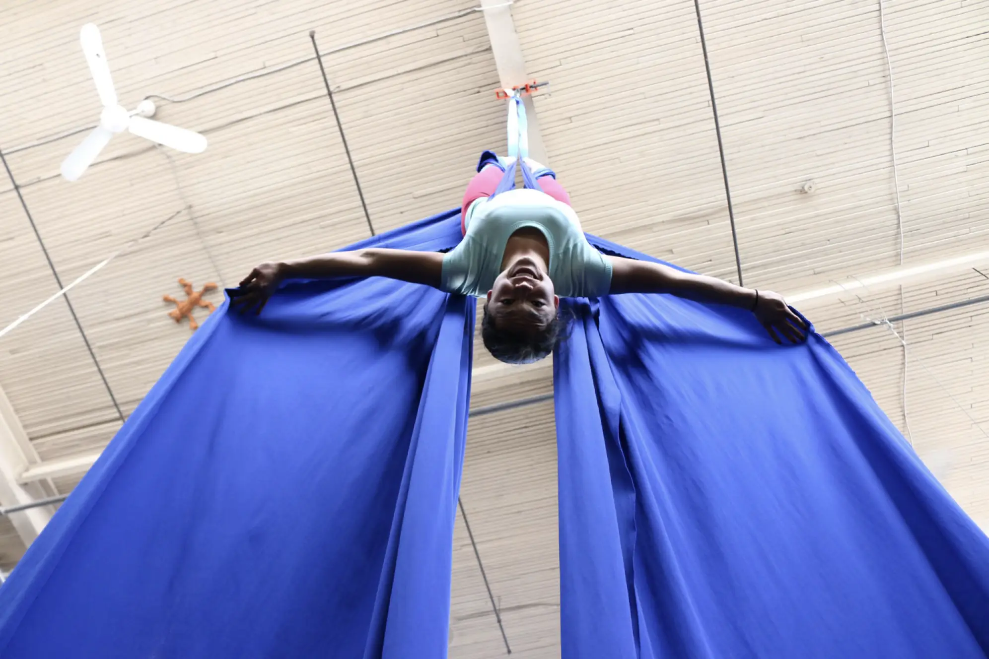 Aerial artist hanging upside down in blue silks and looking at camera