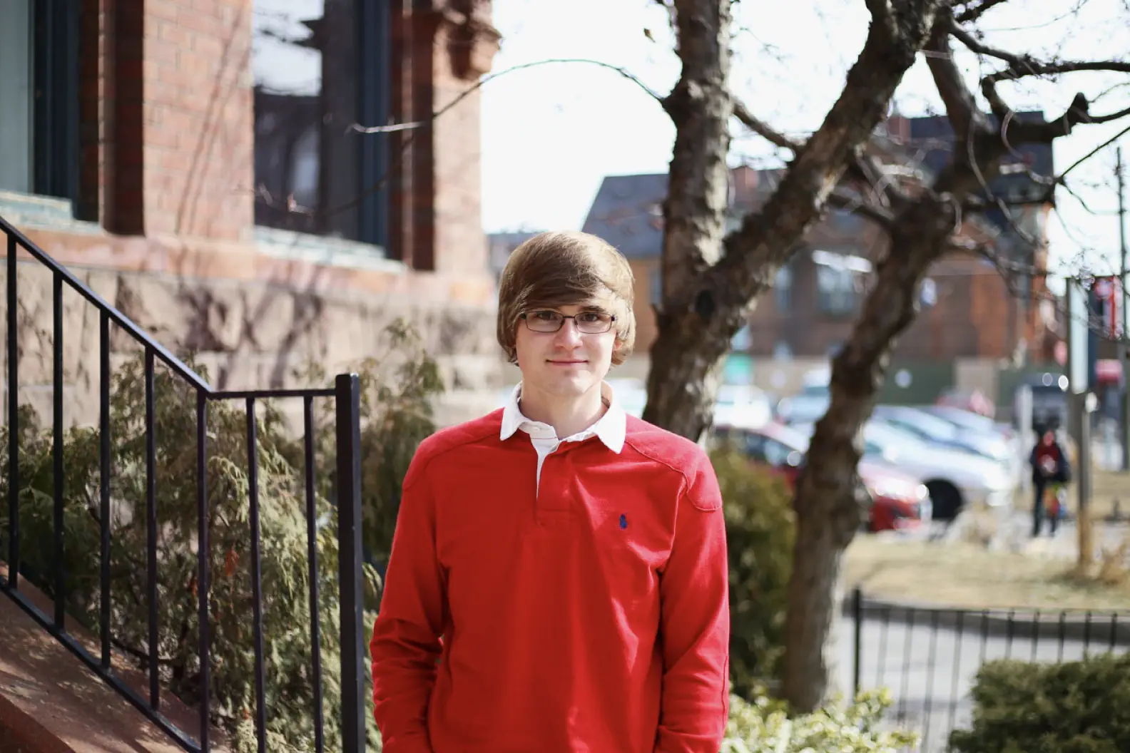 Young man with glasses and red shirt standing outside and smiling at the camera
