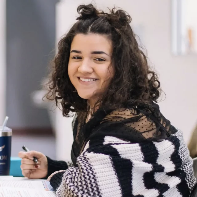 Young person in striped sweater sitting at table and smiling at the camera