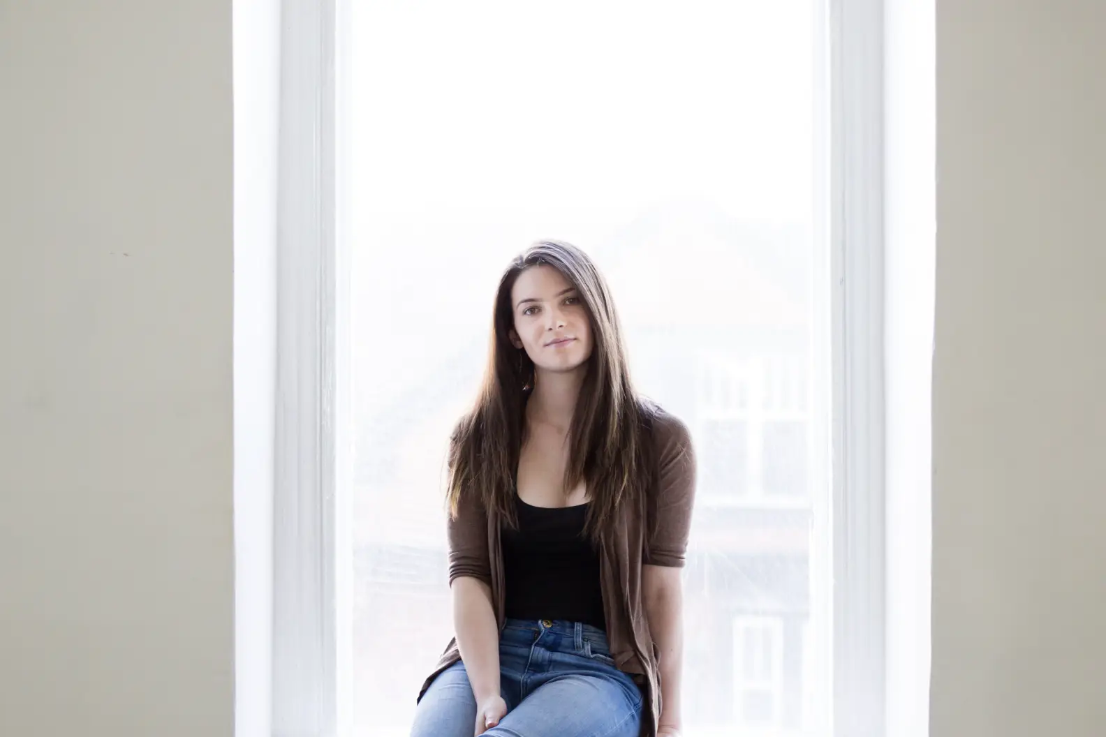 Young woman in sweater sitting in window sill smiling
